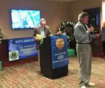 A man speaking into a microphone beside a podium with a chapter banner
