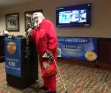 A man dressed as Santa with a cane at the podium beside a chapter banner