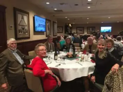 Members smiling at a round table, more tables behind them