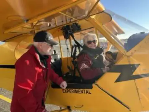 A man in a red jacket beside a yellow Cub with its door open