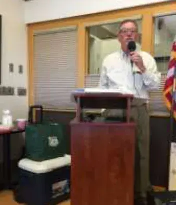 Man speaking into a microphone at a podium beside an American flag