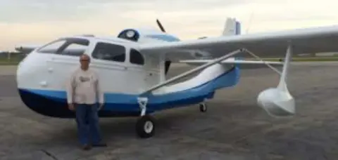 A man standing in front of a white and blue amphibious airplane