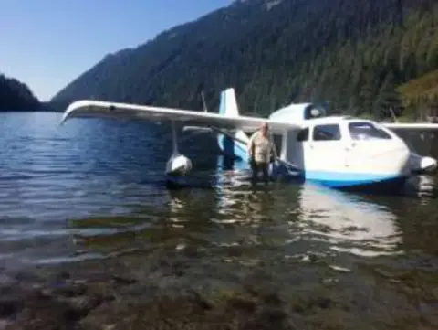 A white and blue amphibian sitting in shallow water by a lakeshore