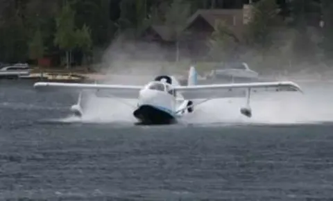 A white and blue amphibian taking off from a lake