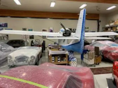 A white airplane and a classic car in a hangar