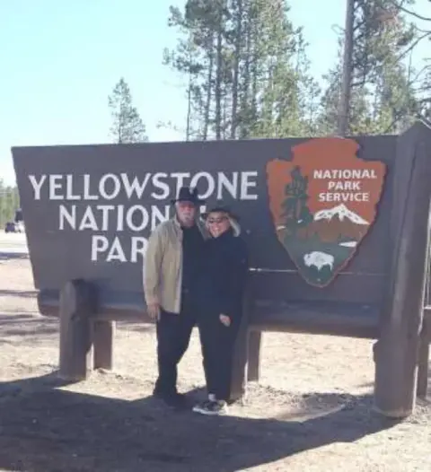 Two people standing at the Yellowstone National Park sign