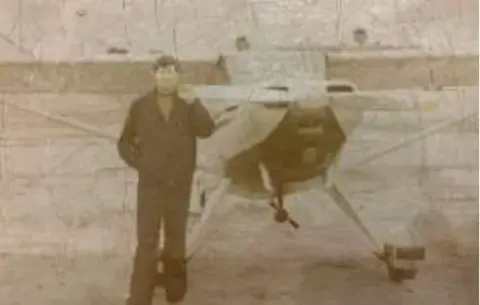 An old sepia photo of a man in front of an airplane