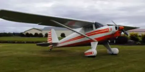 A white and red high-wing airplane on the grass