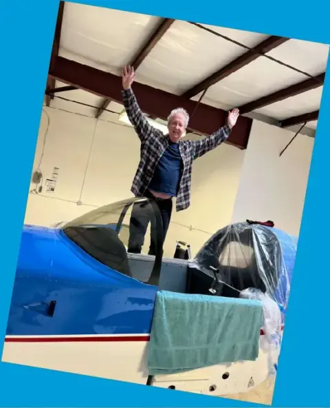 A member standing on the club airplane with his arms raised