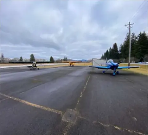 Small airplanes taxiing on a wet runway with trees behind