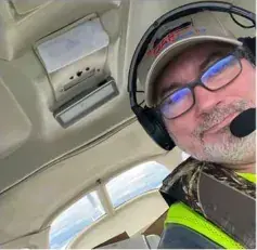 A man in a headset and safety vest taking a selfie in the cockpit