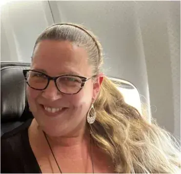 A smiling woman in glasses seated in an airliner cabin