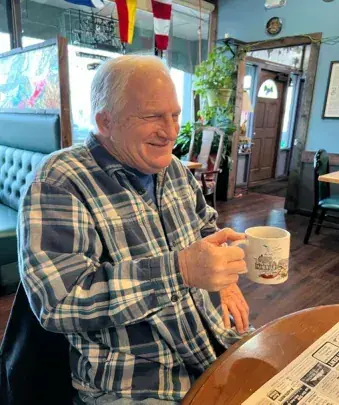An older man in a plaid shirt holding a coffee mug in a cafe