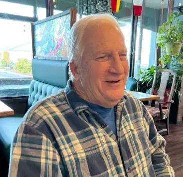 A smiling older man in a plaid shirt in a cafe