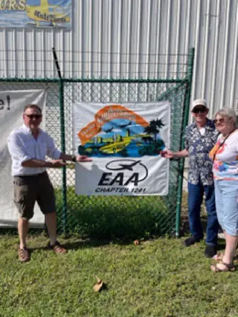 Three people holding an EAA Chapter 1281 banner on a fence