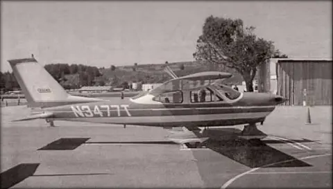 A black and white photo of a high-wing airplane on the ramp
