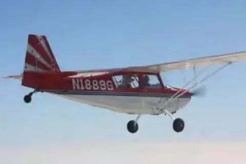 A red and white high-wing airplane, N1889G, in flight