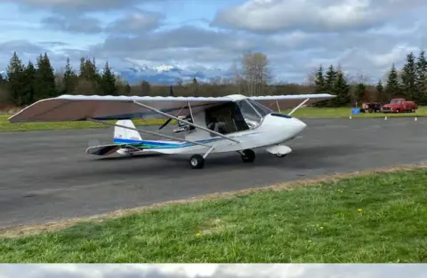 A white high-wing airplane taxiing on the ramp