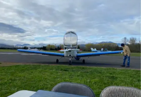 A white low-wing airplane with its canopy open on the ramp
