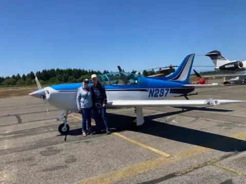 Two people beside a blue and white low-wing airplane