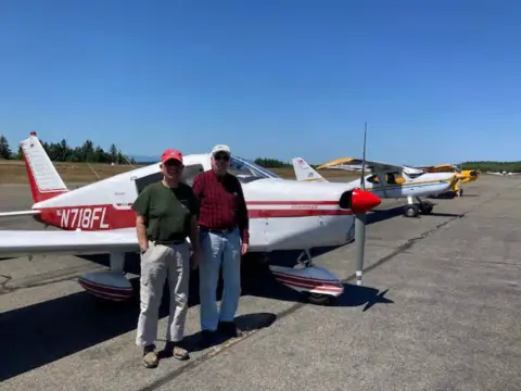 Two men beside a red and white low-wing airplane, N718FL