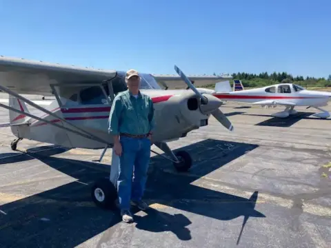 A man in a green shirt beside a white high-wing airplane