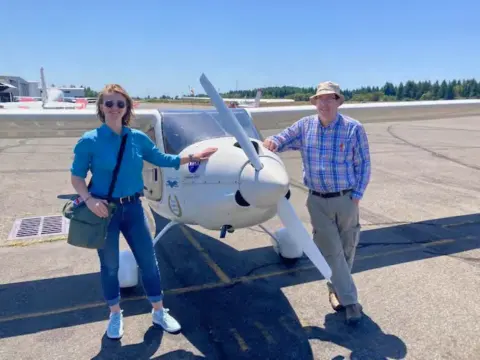 A woman and a man beside a white low-wing airplane