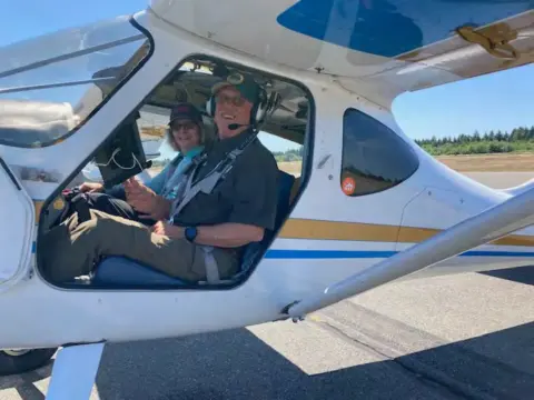 Two people seated in the cockpit of a white airplane with the canopy open