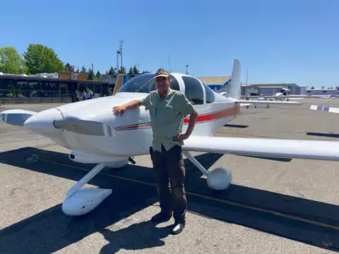 A man in a green shirt beside a white low-wing airplane