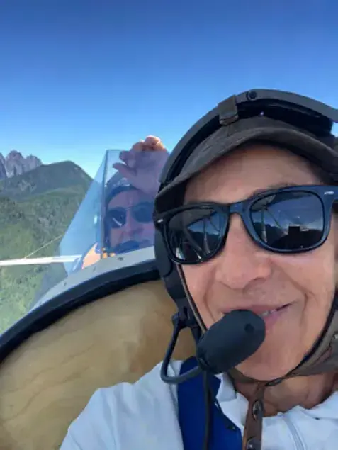 A smiling pilot in sunglasses and a headset in flight