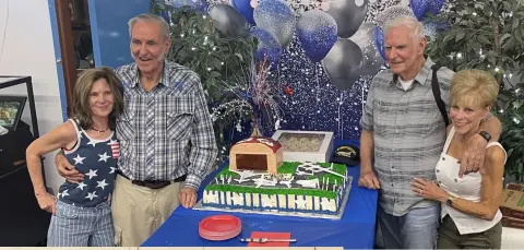 Two couples posing by a birthday cake shaped like an airplane