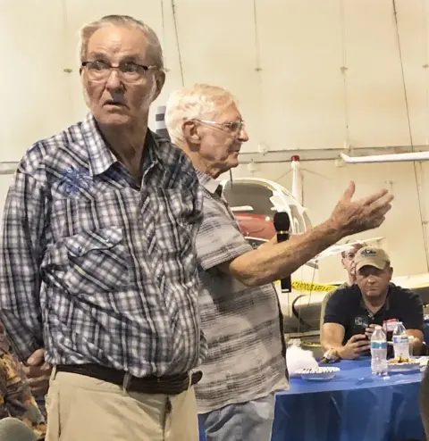 Two older men talking at a table, one gesturing