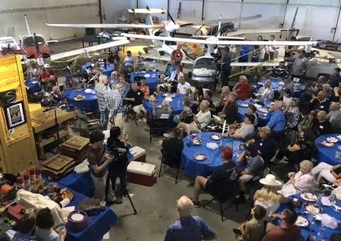 A large crowd seated at tables in a hangar for a presentation