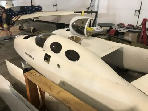 A white composite airplane on display in a hangar
