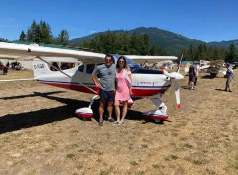 A couple standing by a white high-wing airplane at a fly-in