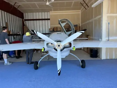 A white composite airplane with a pusher propeller in a hangar