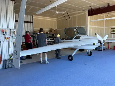 People around a white canard airplane in a hangar