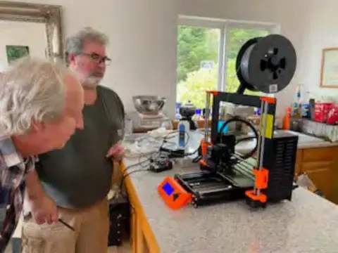 Two men looking at a 3D printer with orange parts