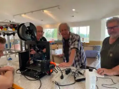 Members working with a 3D printer at a table