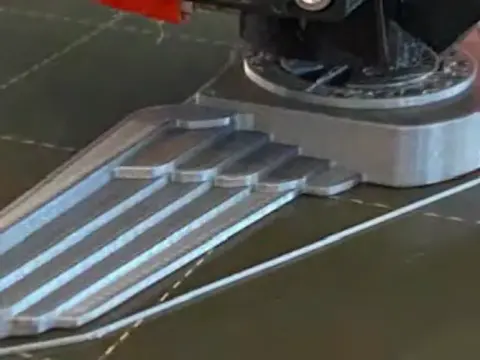 A 3D printed silver wings badge on a printer bed