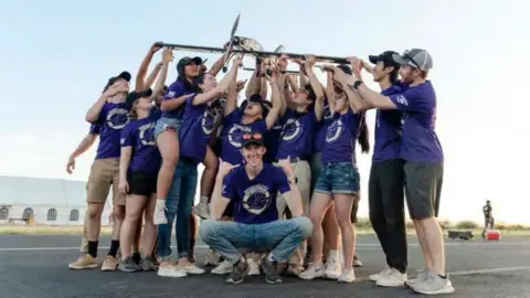 A team of students in purple shirts holding up a small airplane