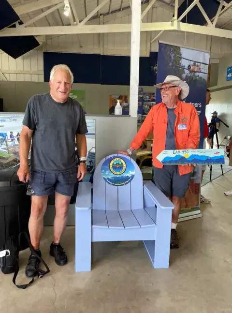 Two men posing with a painted Adirondack chair at an event