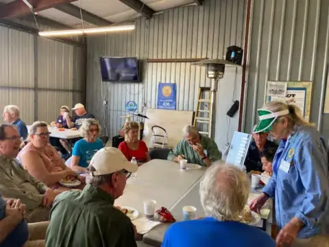 Members seated at tables in a hangar