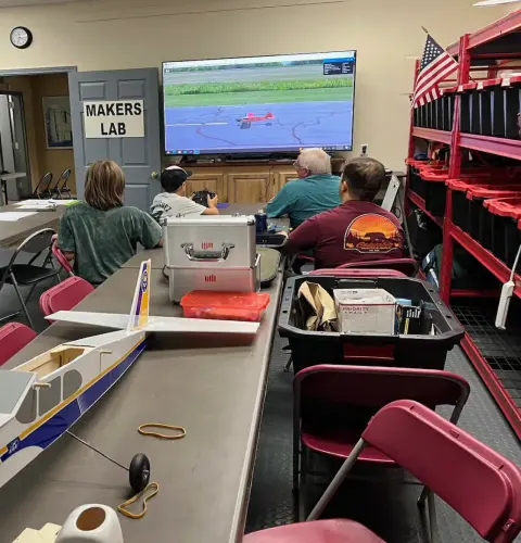 Kids and adults in a Makers Lab classroom watching a flight simulator on a large screen