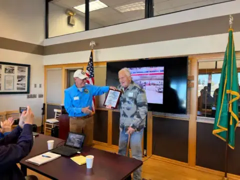 Two men holding a certificate in front of a screen
