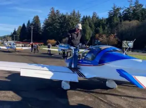 A man climbing into a blue and white low-wing airplane