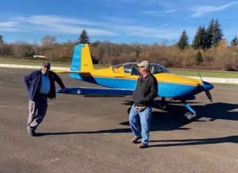 Two men walking beside a yellow and blue low-wing airplane