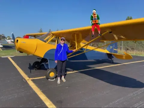A yellow high-wing airplane with a person in a Santa hat on the wing