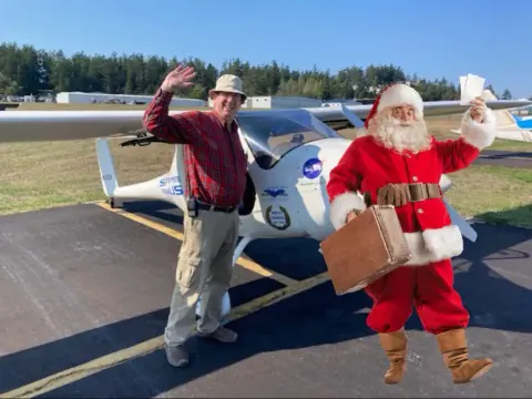 Santa Claus standing with a pilot by an airplane on the ramp