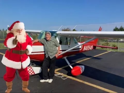 A man dressed as Santa beside a red and white airplane, with another man